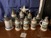 Overview of nine beer steins with ornate pewter lids and colorful designs.