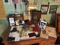 Wide shot of memorabilia collection on wooden desk including decorative wastebasket, framed art, various vintage items and stationery.