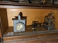 Image showing three navy military items displayed on a wooden shelf: two metal lanterns and one brass sextant instrument.