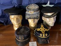 Full view of 5 military hats on mannequin heads showing variety including U.S. Navy and Confederate styles.