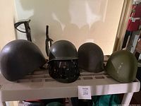Five helmet shells arranged side by side on a plastic shelf, two modern helmets flank three steel shells
