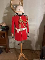 Full front view of red British military dress uniform on wooden stand with pith helmet.