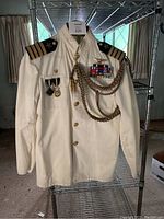 Full front view of white naval dress jacket showing shoulder boards, buttons, ribbons, medals, aiguillette