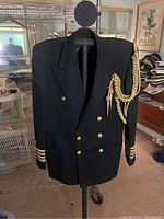 Navy officer jacket hanging on stand showing front buttons, gold braid on shoulder, and sleeve stripes.