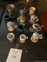 Top view photo of 11 assorted shot glasses and mini steins on black table showing size and arrangement