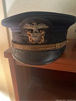 Front perspective of the black WWII US Navy officers cap showing insignia and leather visor.