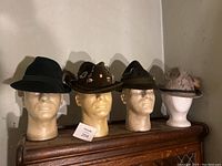 Four vintage fedora hats mounted on styrofoam heads, showing full front view of each hat in a row on a wooden surface.