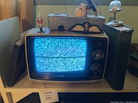 Vintage Sharp black and white television showing static screen with two large books on either side, model vehicle with fishing rod and decorative items on top.