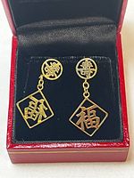 Pair of 14 KT yellow gold Chinese character earrings displayed in a red and black jewelry box showing front face with circular and square shapes with Chinese characters.