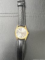Front view of Casio men's watch with black leather strap and gold-tone case on textured surface showing dial and strap