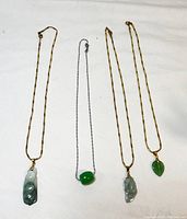 Four carved natural stone pendants displayed with their chains on white background, showing size and color variations.