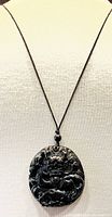 Close-up of dark green jade dragon carved pendant showing detailed carving and glossy finish, hanging on black cord.
