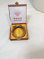 Natural jade bangle bracelet in red display box with yellow satin lining.