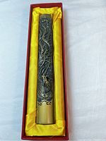 Brass paperweight in red box with yellow satin lining showing detailed peacock relief and calligraphy design.