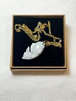 Overall view of the jade fish pendant necklace with gold tone chain displayed in box with black velvet interior.