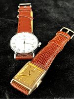 Top view showing both watches side by side on black background, Seiko watch has gold square dial, Geneva watch has white round dial with Roman numerals.