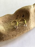 Pair of solid gold earrings with round faux diamonds, shown from the front on a wooden surface.