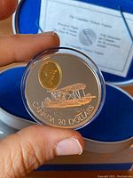Close-up of aviation-themed side of coin with vintage seaplane and gold inset portrait, held in hand in front of blue velvet interior box lining.