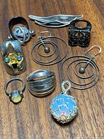 Collection of Mid-Century Modern sterling silver jewelry items arranged on wooden surface including rings, earrings, and pendant, showing detailed views of each piece's design and stones.