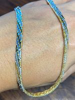 Close-up showing braided mesh woven texture combining sterling silver and gold on the necklace draped on hand.