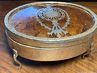 Front angle view of the oval-shaped sterling silver and tortoiseshell vanity box with ornate feet and silver medallion on lid.