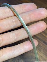 Close-up of the gold tone side of the omega style necklace held on fingers showing texture and finish.