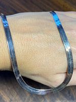 Close-up photo showing the silver side of the flat herringbone necklace worn on a wrist.