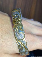 Close-up photo of the sterling silver bangle bracelet with gold floral carving and textured pattern on wrist.
