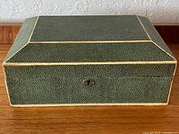 Front view of the rectangular shagreen box, showing the keyhole and cream piping on the green textured surface