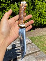 Knife held in hand showing stag style handle and polished blade with engraving.