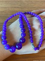 Full view of the necklace draped over a hand showing the graduated bead sizes and sheen of lavender jade.