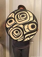 Front view of circular wooden plaque with high-relief Northwest Coast design held by person to show scale
