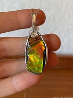 Front view of the pendant showing iridescent ammonite/ammolite specimen in sterling silver wire wrapped setting held between fingers.