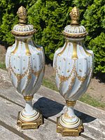 Front view of both white porcelain urns with gold gilt decoration on tabletop
