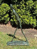 Full side view of tall humanoid sculpture walking pose outdoors