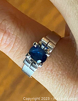 Close-up of ring on finger showing oval blue sapphire and setting
