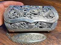 Overall front and top view of rectangular dragon filigree clutch showing openwork design and chain strap attached.