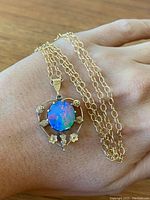 Hand holding gold-tone pendant necklace displaying round opal center and chain draped on skin