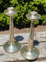 Front angle view of both candlesticks on wooden surface against greenery background