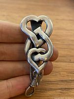 Front view of the sterling silver heart-shaped buckle/clip held by hand, showing intertwined heart design.