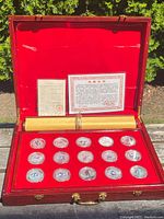 Open mahogany‐tone wooden case lined in red velvet showing 15 coin capsules and space for scroll and certificate