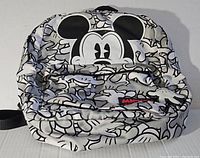Full front view of white and black Disney backpack with large Mickey Mouse face and front zipper pocket.