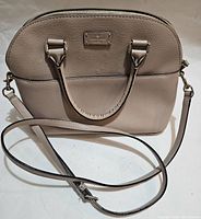 Light taupe Kate Spade handbag with dual top handles, curved top zipper, and detachable strap laid flat, shown fully in photo.