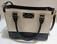 Front view of the Kate Spade black and white leather shoulder bag with gold logo plate and dual handles.