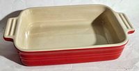 Top and angled view of red ceramic rectangular casserole dish with cream interior showing handles and interior condition.
