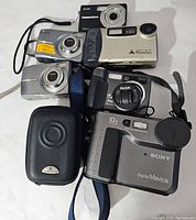 Top view showing all six cameras, highlighting diverse brands and styles including Sony Digital Mavica, Kodak models, Minolta PhotoCam, and Samsung carrying case.