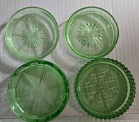 Top-down view of four uranium glass coasters showing various starburst and textured patterns on the clear green glass surfaces.