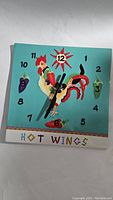 Front view of colorful square clock with rooster and chili pepper design on turquoise background, showing clock face and hands.