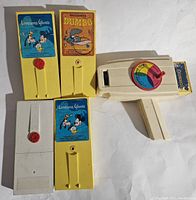 Four vintage Fisher Price movie reels with Lonesome Ghosts, Dumbo, and Cinderella labels, some in yellow and white plastic holders, displayed with the movie viewer.