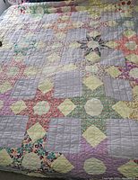 Full view of vintage patchwork quilt showing multiple star-shaped patch blocks and square patches in warm pastel colors and florals.